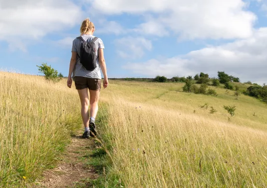 Woman walking through a field of tall weeds in a valley