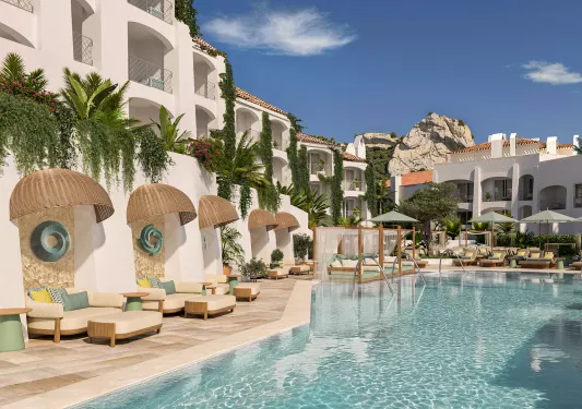 Outdoor pool with a white hotel building in the background and cushioned sofas surrounding the pool
