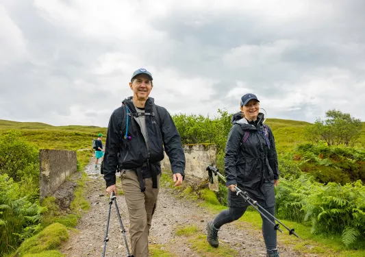 Man and woman holding hiking poles, walking on a dirt trial