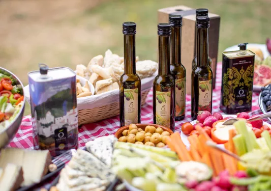 Table full of vegetables and snacks, and 5 bottles of olive oil