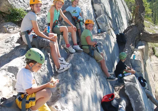 Group of kids sitting on a large boulder with climbing gear on