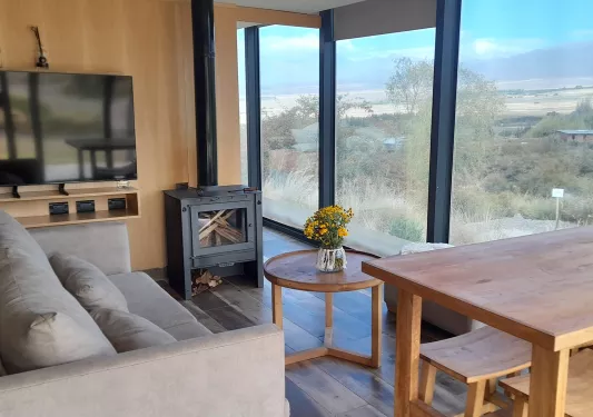Couche with a wooden table and metal fireplace, looking out towards a glass wall with a valley outside
