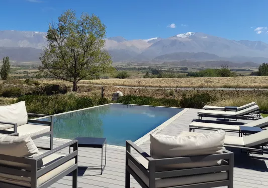 Outdoor pool surrounded by white, cushioned chairs in a valley with mountains in the background