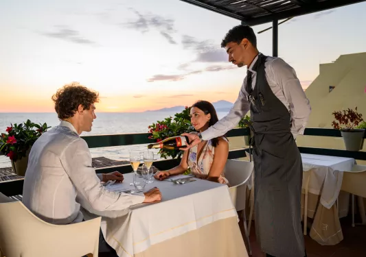 Man and woman dining at a table, with a waiter pouring wine into two glasses