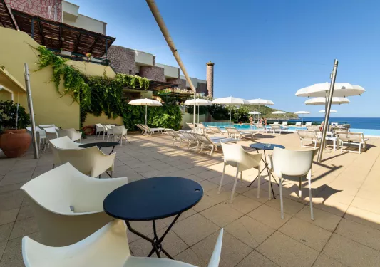 Outdoor patio with beige chairs in front of black tables, with a stone building in the background