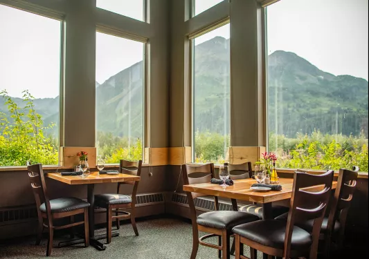 Dining room with two square tables and tables next to windows, looking out to large mountains