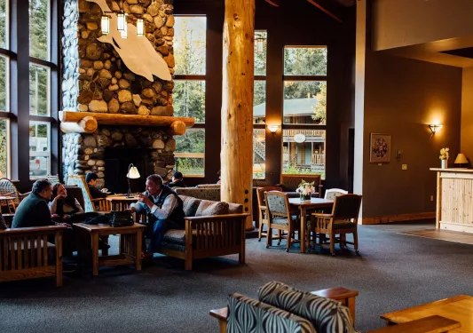 Cabin lobby with large wooden pillars and people sitting in front of a stone fireplace