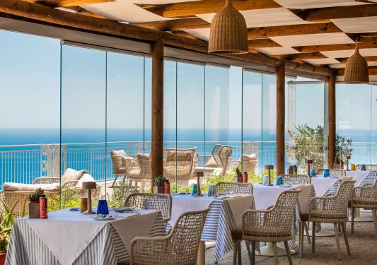 Indoor dining area with large, glass walls looking out to a balcony by the beach