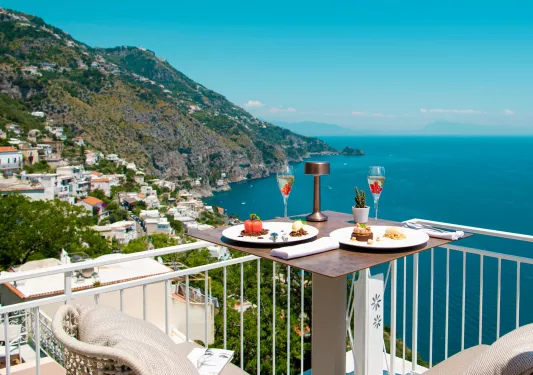 Outdoor balcony with a table full of food, looking out towards the ocean and hills