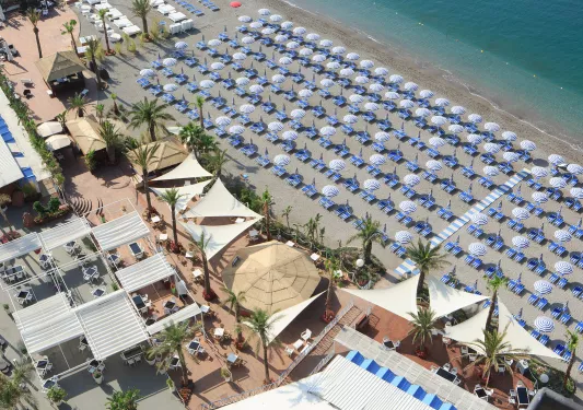Sky view of a beach with white and blue chairs and umbrellas lined up on the sand