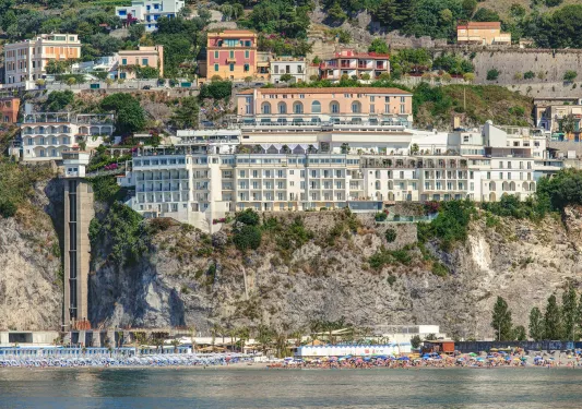 Exterior view of large hotel complex on a cliff, with the beach on the ground level