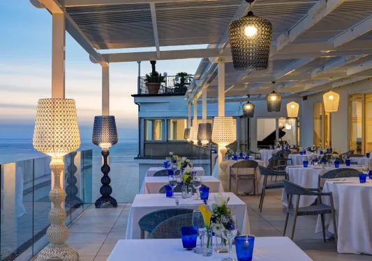 Outdoor patio and dining area, with wine glasses on each table and light fixtures surrounding the tables