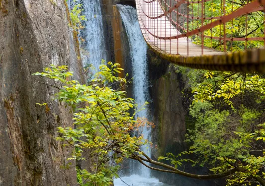 View of a long, wooden bridge over an active waterfall