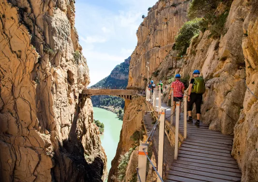 Group of people walking on a wooden bridge in between two large cliffs