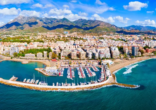 Sky view of a town in front of a beach, with large mountains in the background