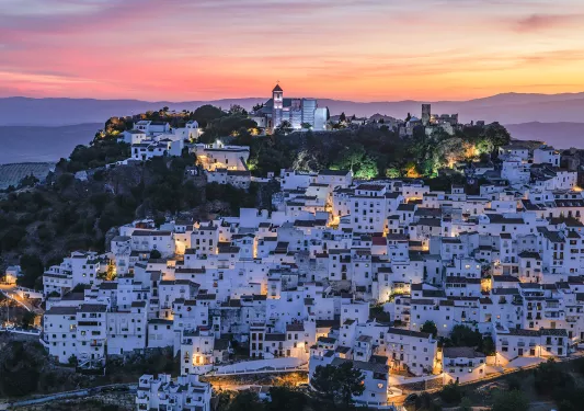 Sky view of a cluster of white houses on a cliff with the sunset in the distance