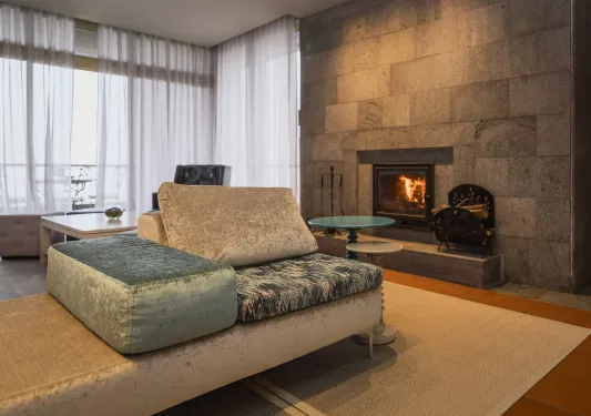 Corner room with cushioned, velvet couches in front of a stone fireplace