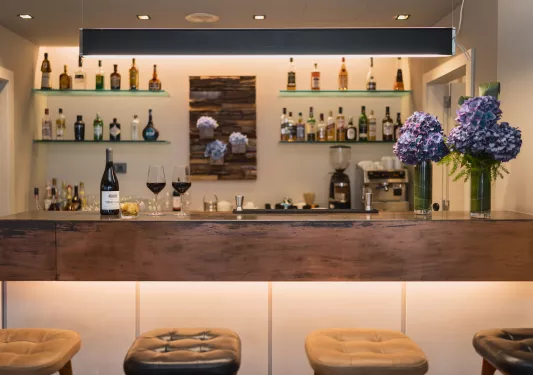 Bar counter with alcohol on the shelves along the wall and cushioned stools in front