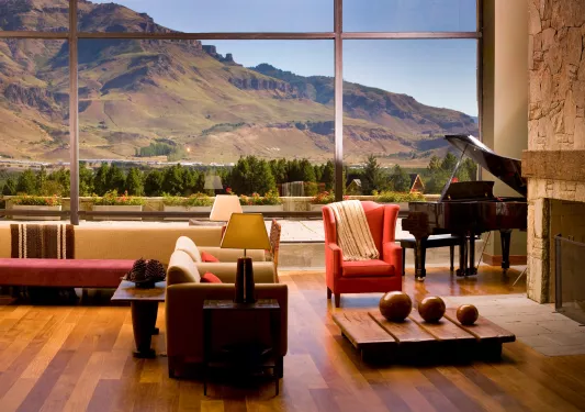 Indoor lobby with cushioned chairs, with large windows looking out to tall hills