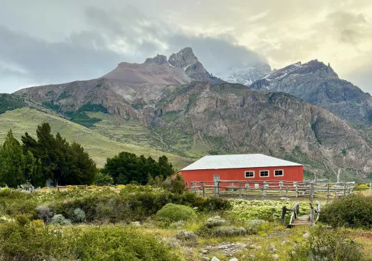 Red barn building in the middle of a grassy valley, with large mountains in the background