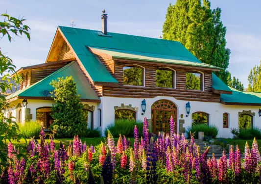 Cabin-style house with a green roof and pink flowers in front