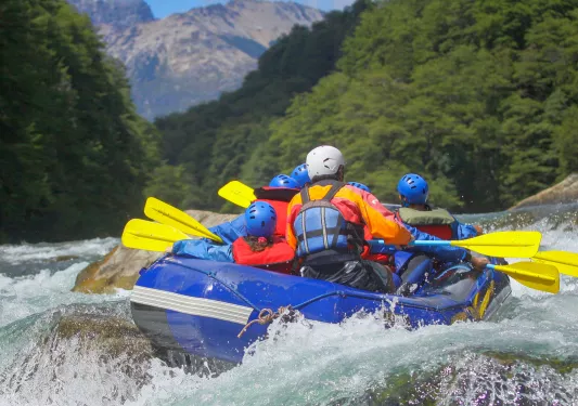 Group of people on a blue raft, paddling through an active river