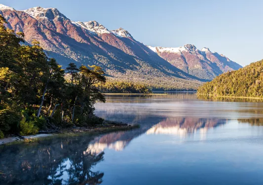 Open lake, surrounded by tall trees and snow-capped mountains