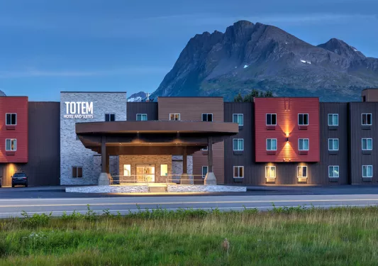 Exterior view of red, black and brown hotel buildings with large mountains in the background
