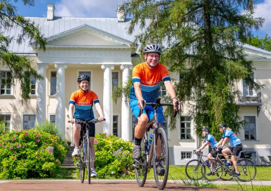 Two couples of men and women smiling while biking in front of a large, white building