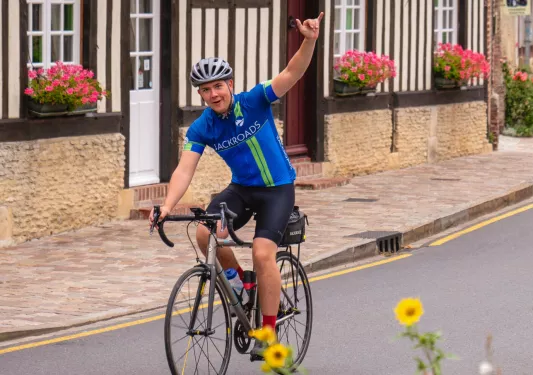 Man smiling while riding a bike on a road with one arm up