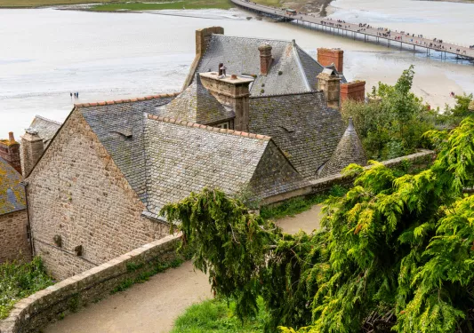 Top view of a stone building, with a dirt road and a large lake in the background