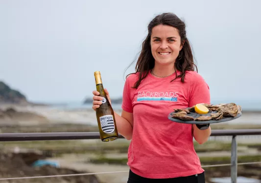 Woman in a pink shirt, holding a bottle of wine and a plate of oysters