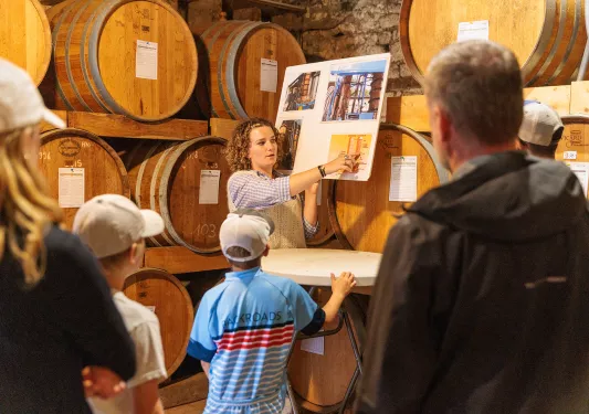 Woman in a wine cellar, holding up a poster board presenting to a group of guests