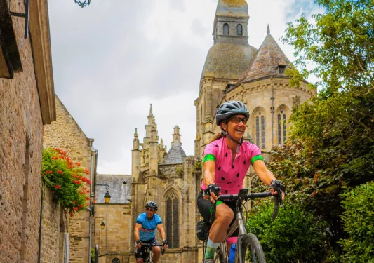 Man and women riding bikes on a stone path, with a cathedral in the background