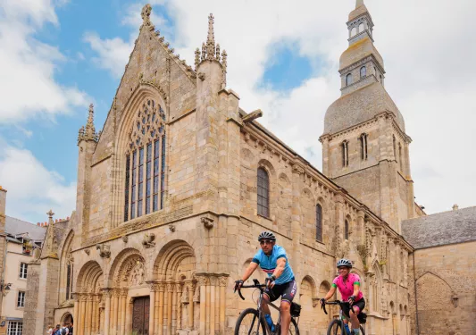 Man and woman biking in front of a stone cathedral
