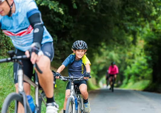 Kid smiling while riding a bike on a road surrounded by trees