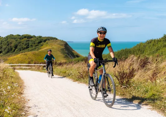 Man and woman biking on a sandy trail with the ocean in the background