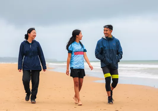 Two women and one man smiling while walking on a beach