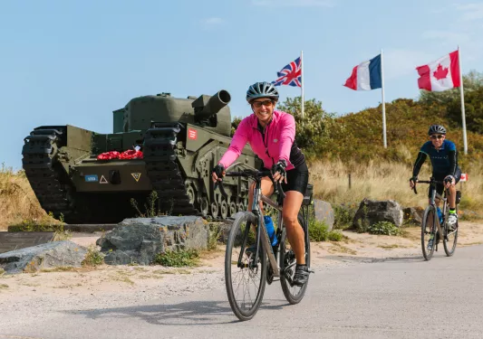 Woman in pink, biking in front of a green tank with flags waiving in the background
