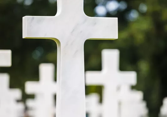 A white cross memorial with a small American flag sticking out from the ground