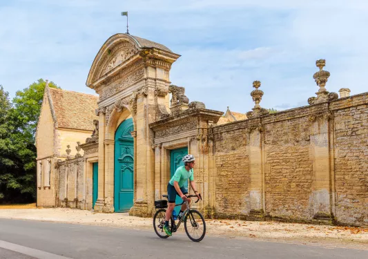 Man in green biking in front of a large stone palace entrance