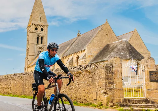 Man wearing sunglasses, riding a bike in front of a stone cathedral