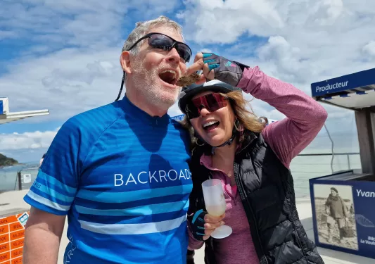 Man and woman smiling while holding up an oyster to eat