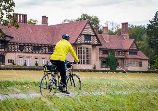 Person wearing a yellow jacket, riding a bike with a large building in the background
