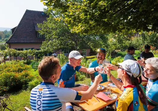 Group of people sitting at a table outdoors, raising their glasses of drinks