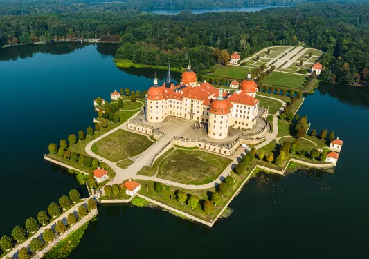Sky view of large yellow and brown building, surrounded by a body of water