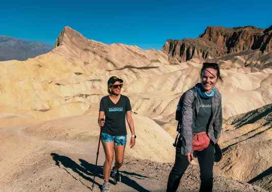 Two women ascending a rocky trail with large canyons in the background