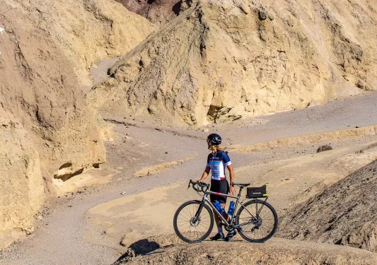 Woman standing next to her bike on a boulder, looking out to large canyons