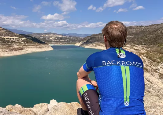 Man sitting on a cliff looking out to a large lake and canyons