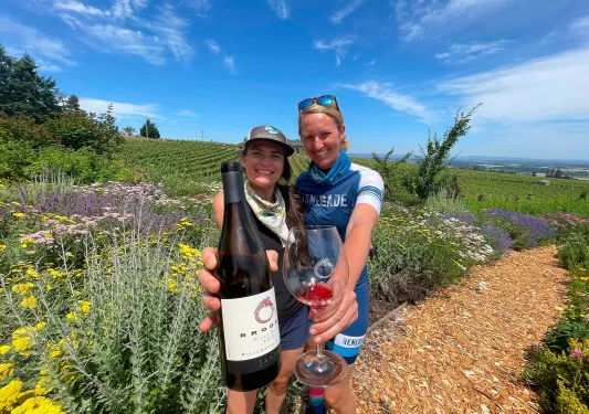 Two women smiling while holding up a wine bottle and wine glass